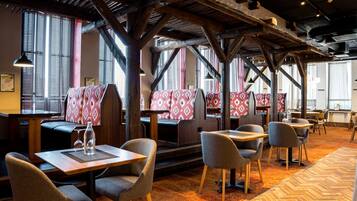 Un restaurant avec des poutres en bois, des banquettes à motifs et des tables avec des chaises.