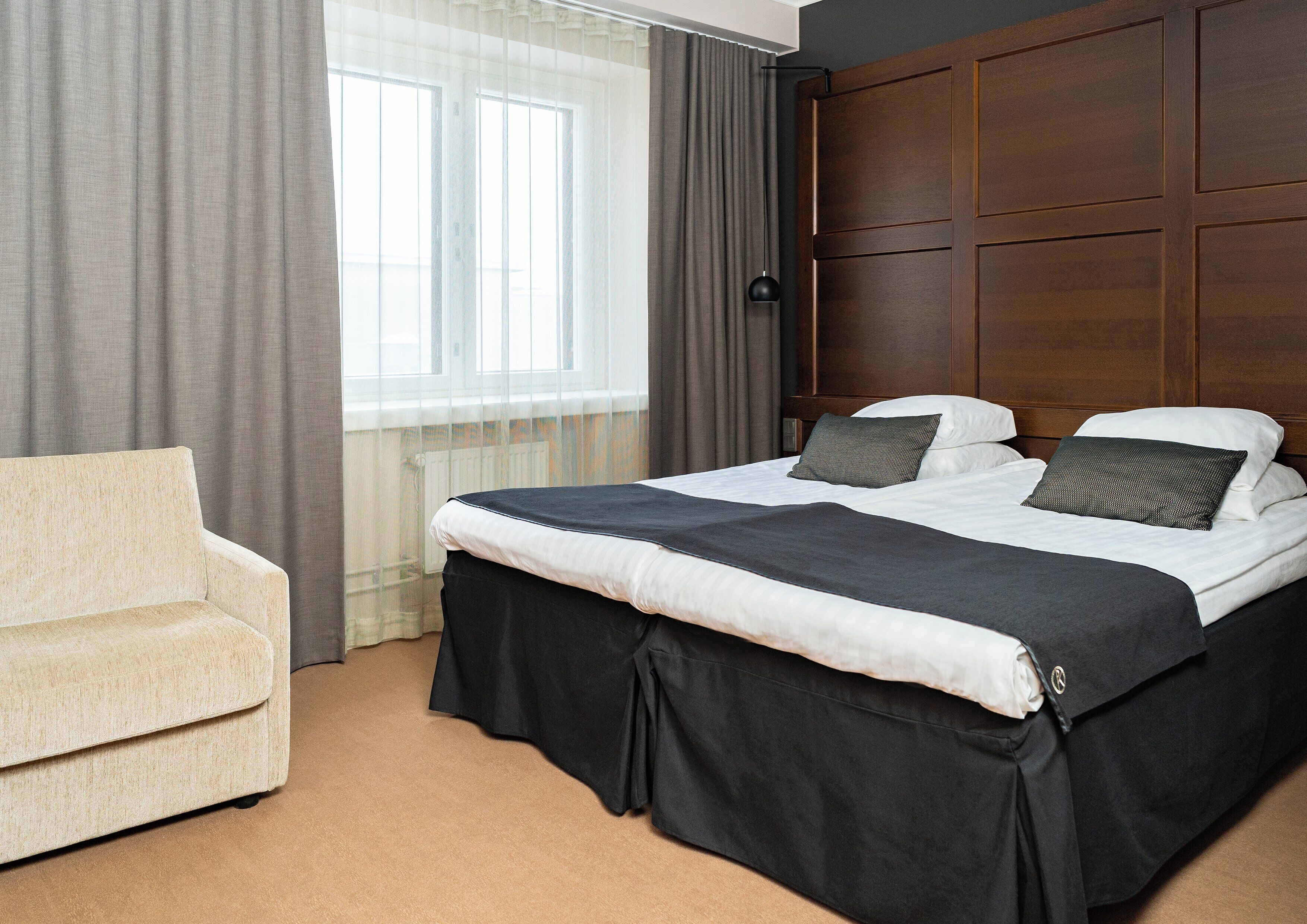 A hotel room with a bed, a chair, and a window with curtains.