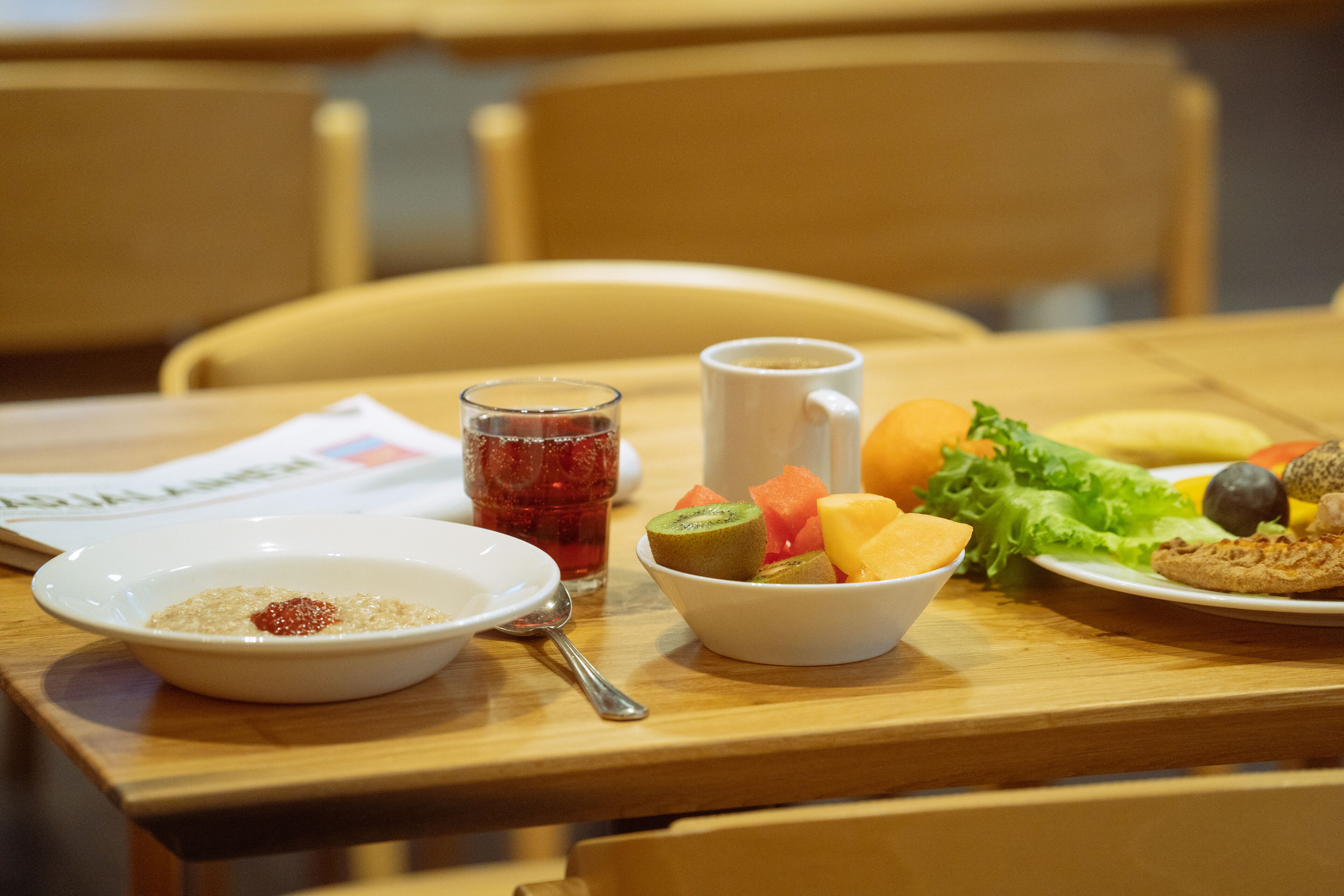 Une table à manger avec un saladier de fruits, une assiette de biscuits, un verre contenant une boisson rouge, une tasse blanche et une cuillère.