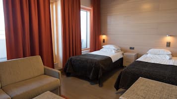 Two single beds with white linens, a comfortable armchair, and a bedside table with a lamp.
