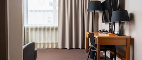 Habitación de hotel con un escritorio de madera, dos lámparas negras, un televisor y un sillón gris.
