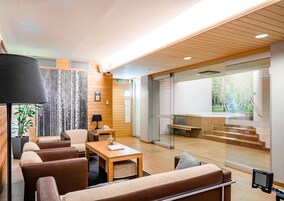 A modern interior with a seating area, a wooden wall, a glass partition, and a view of a pool area.