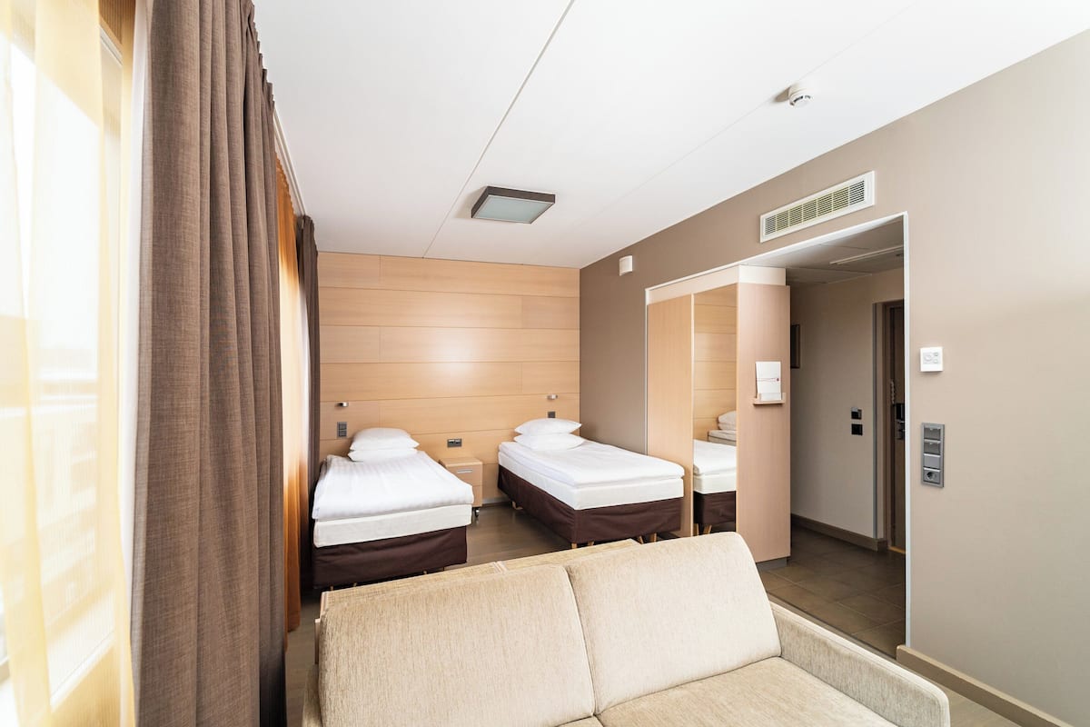 A hotel room with two beds, a sofa, a mirror, and a door leading to a hallway.