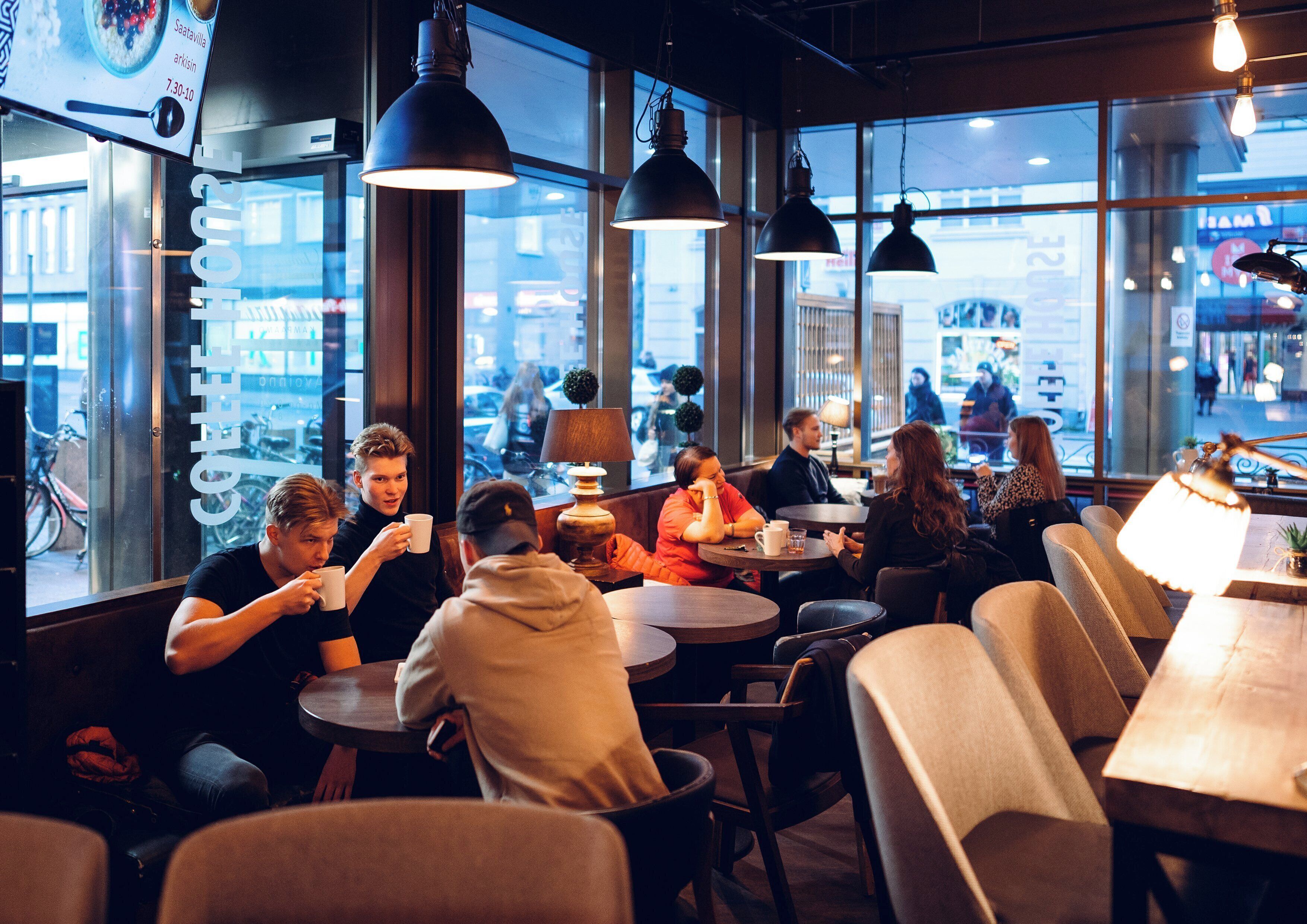 A café with round tables and chairs, large windows, and hanging pendant lights.