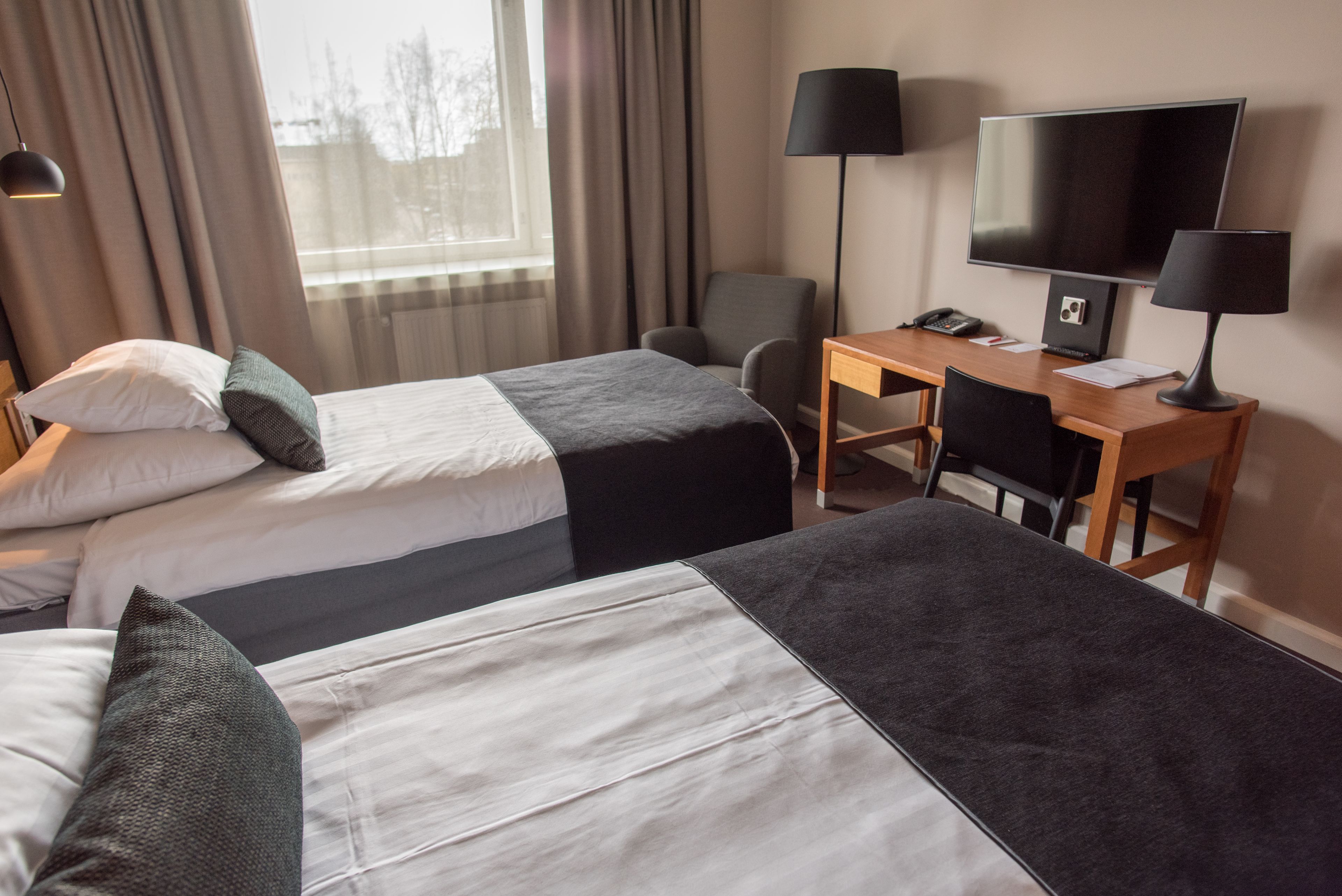 Et hotelværelse med to senge, et skrivebord, en stol, et fjernsyn og en lampe.