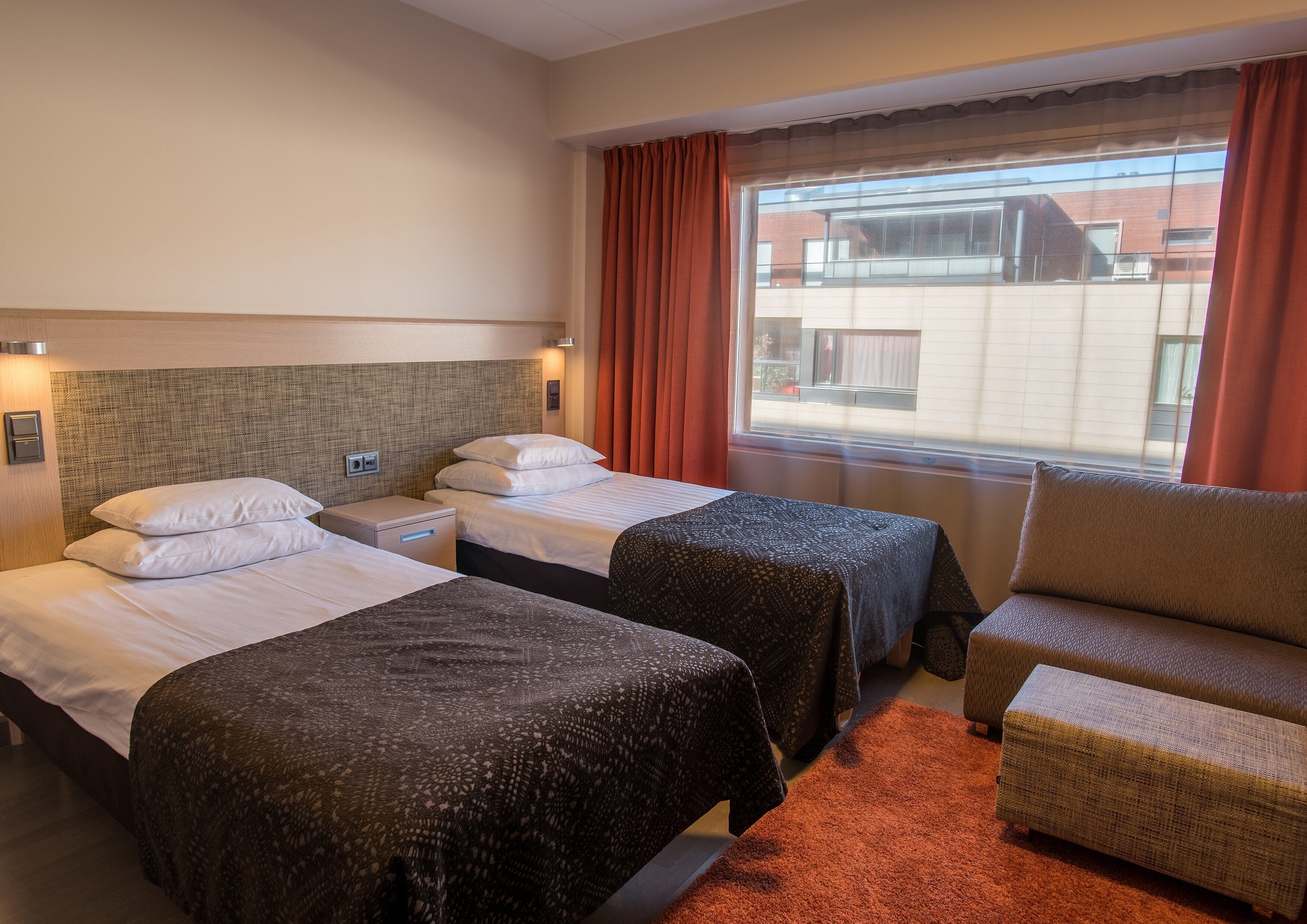 Habitación de hotel con dos camas, un sofá, una ventana con cortinas y vistas al exterior.