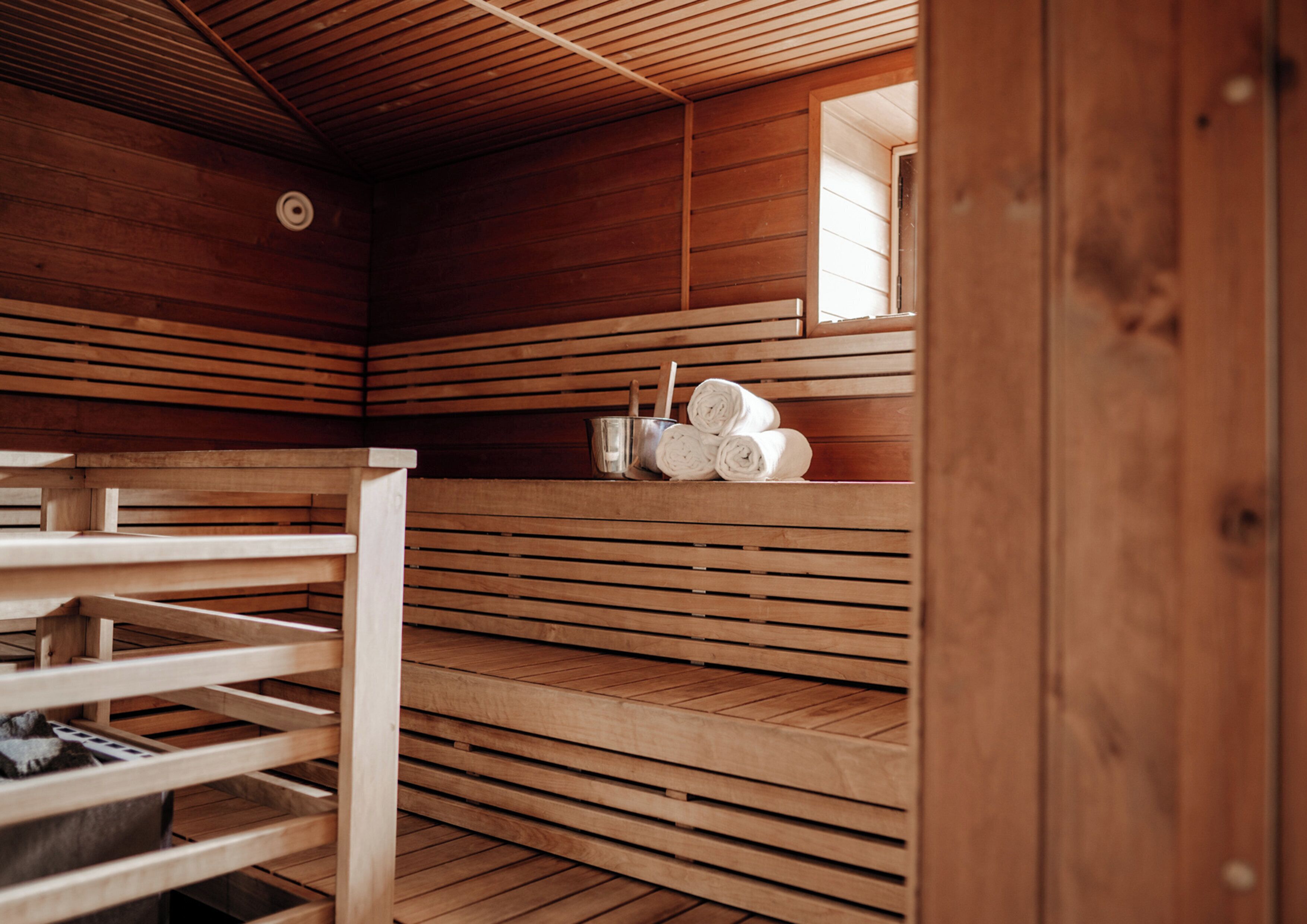 Sauna, jossa on puiset lauteet sekä hylly, jossa on pyyhkeitä ja ämpäri.