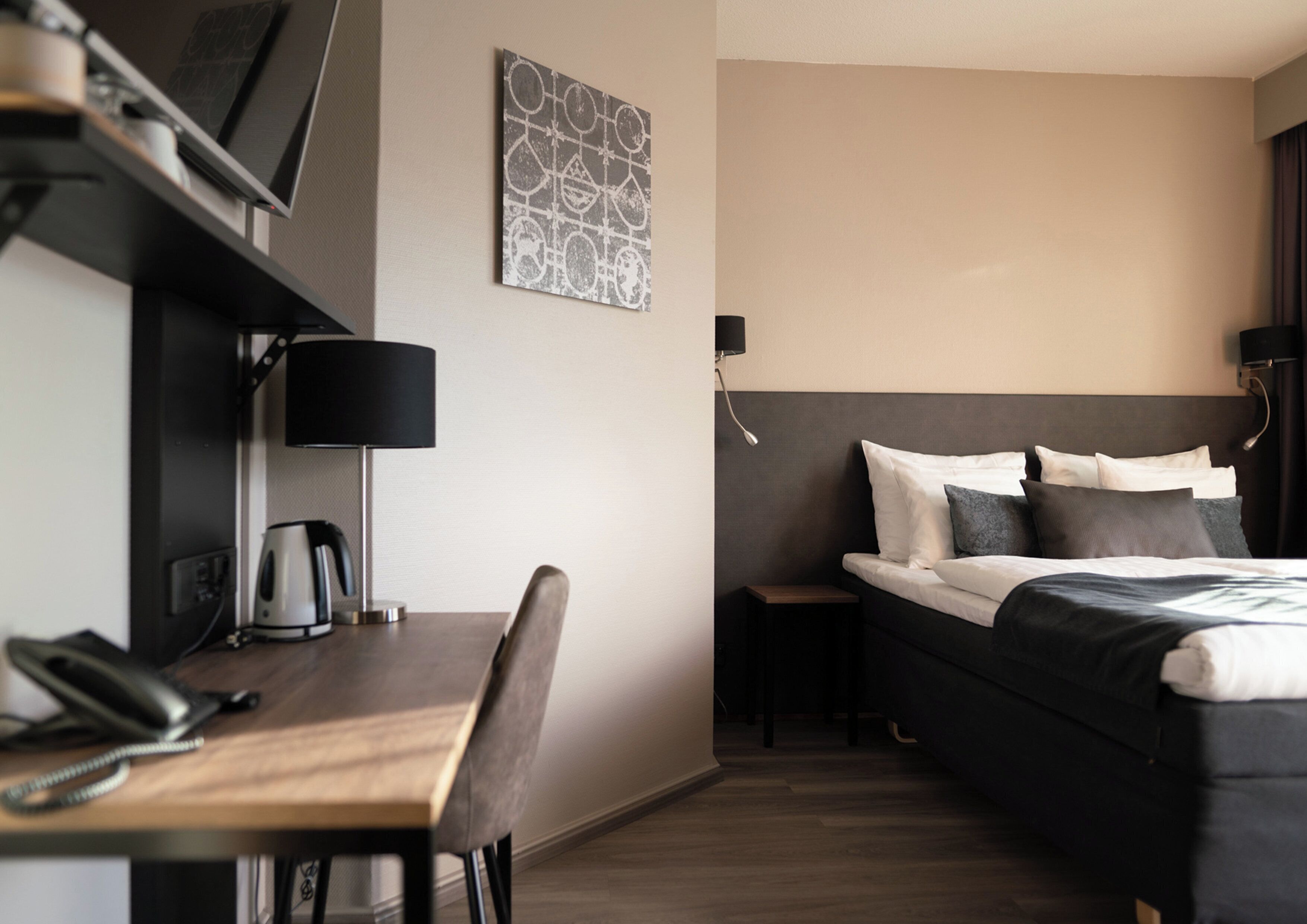 A hotel room with a bed, bedside table, lamp, and a desk with a telephone.