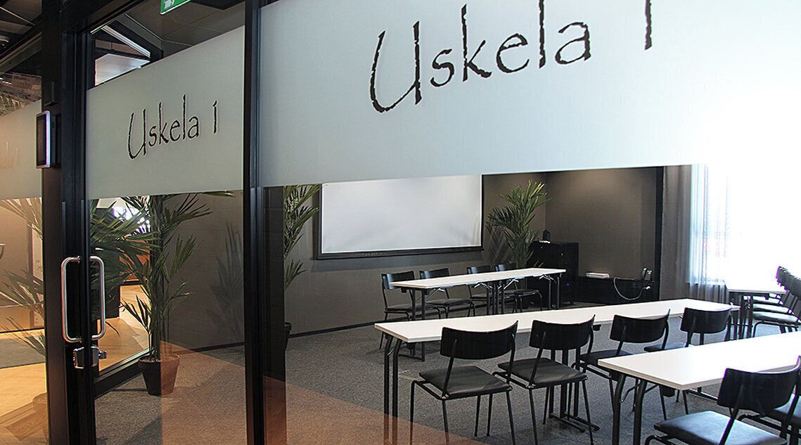 Une salle de conférence équipée de tables et de chaises, d’un tableau blanc et d’un écran de projection.