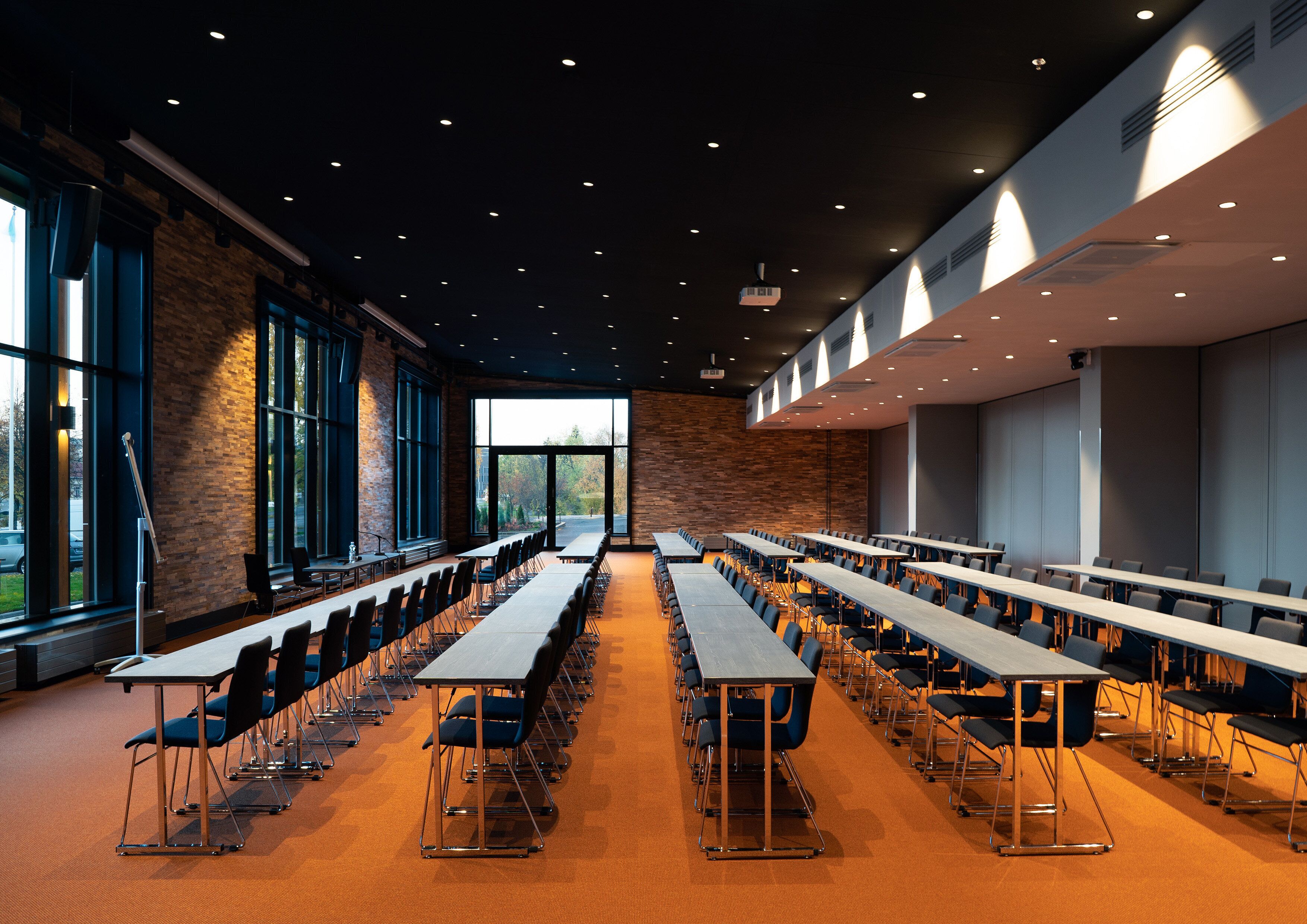 A conference room with long tables and chairs, large windows, and a brick wall.