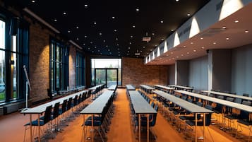 A conference room with long tables and chairs, large windows, and a brick wall.