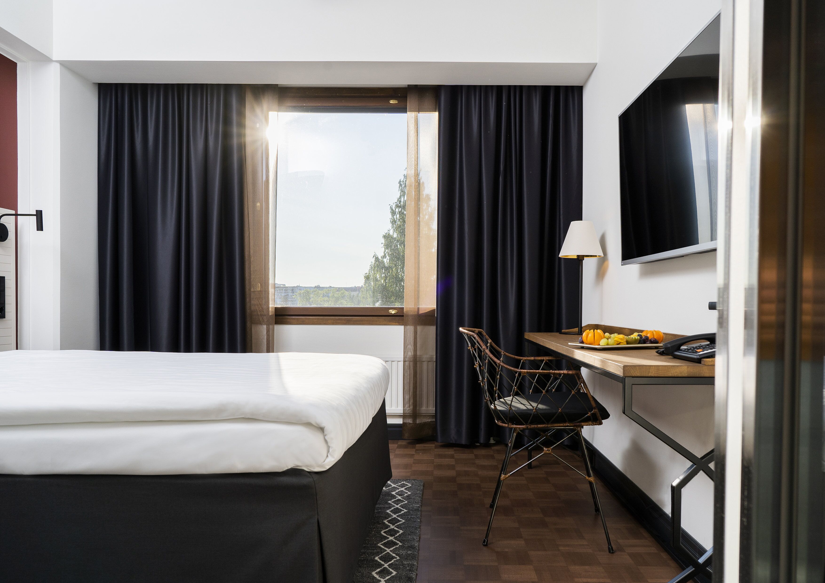 Quarto de hotel com uma cama, uma mesa com abajur, uma cadeira e vista pela janela.