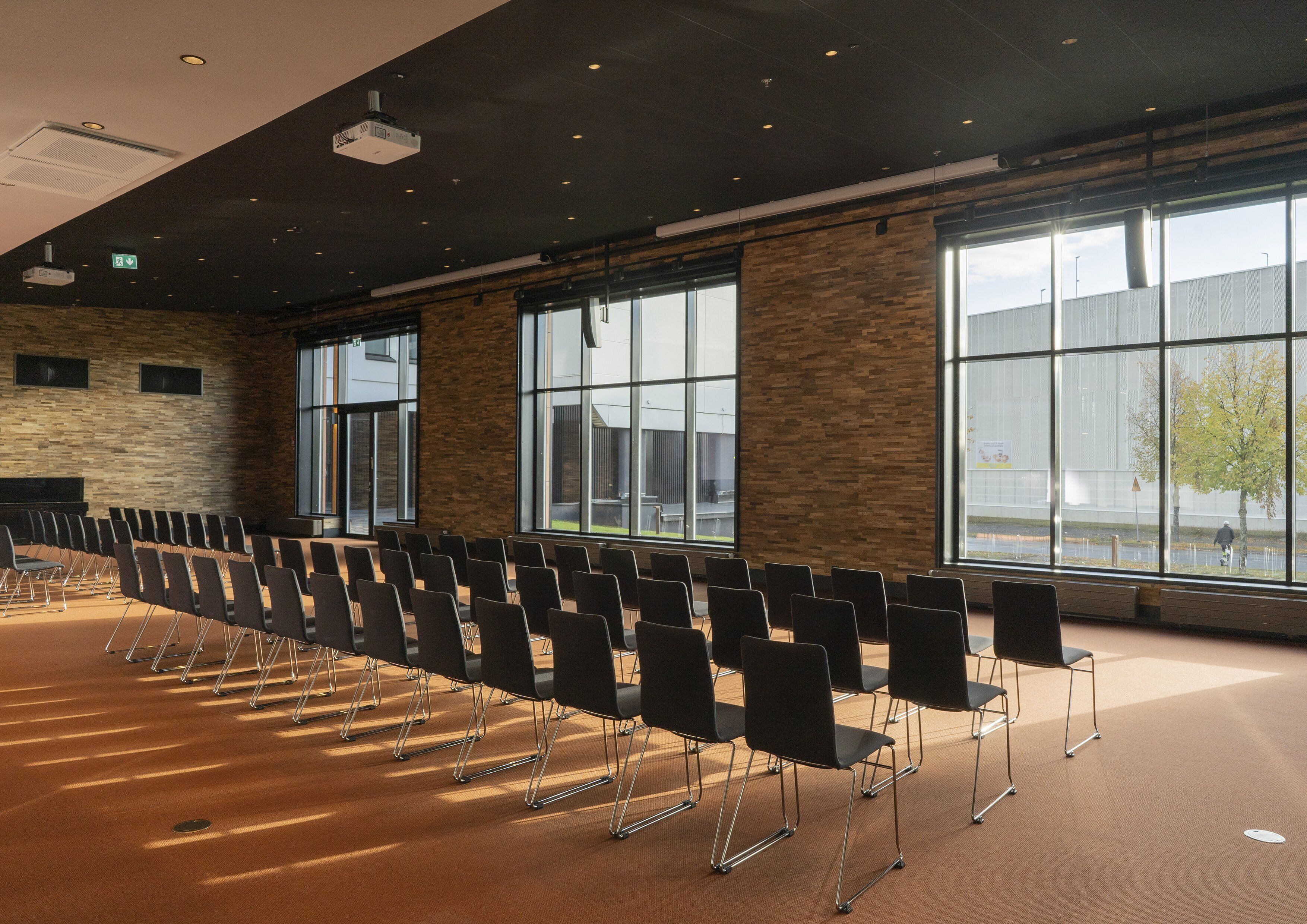 A conference room with rows of chairs, large windows, and a stone wall.