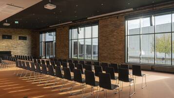 A conference room with rows of chairs, large windows, and a stone wall.