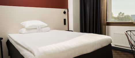 Una cama bien hecha con sábanas blancas, cabecera negra y ventana con vistas a árboles y un edificio.