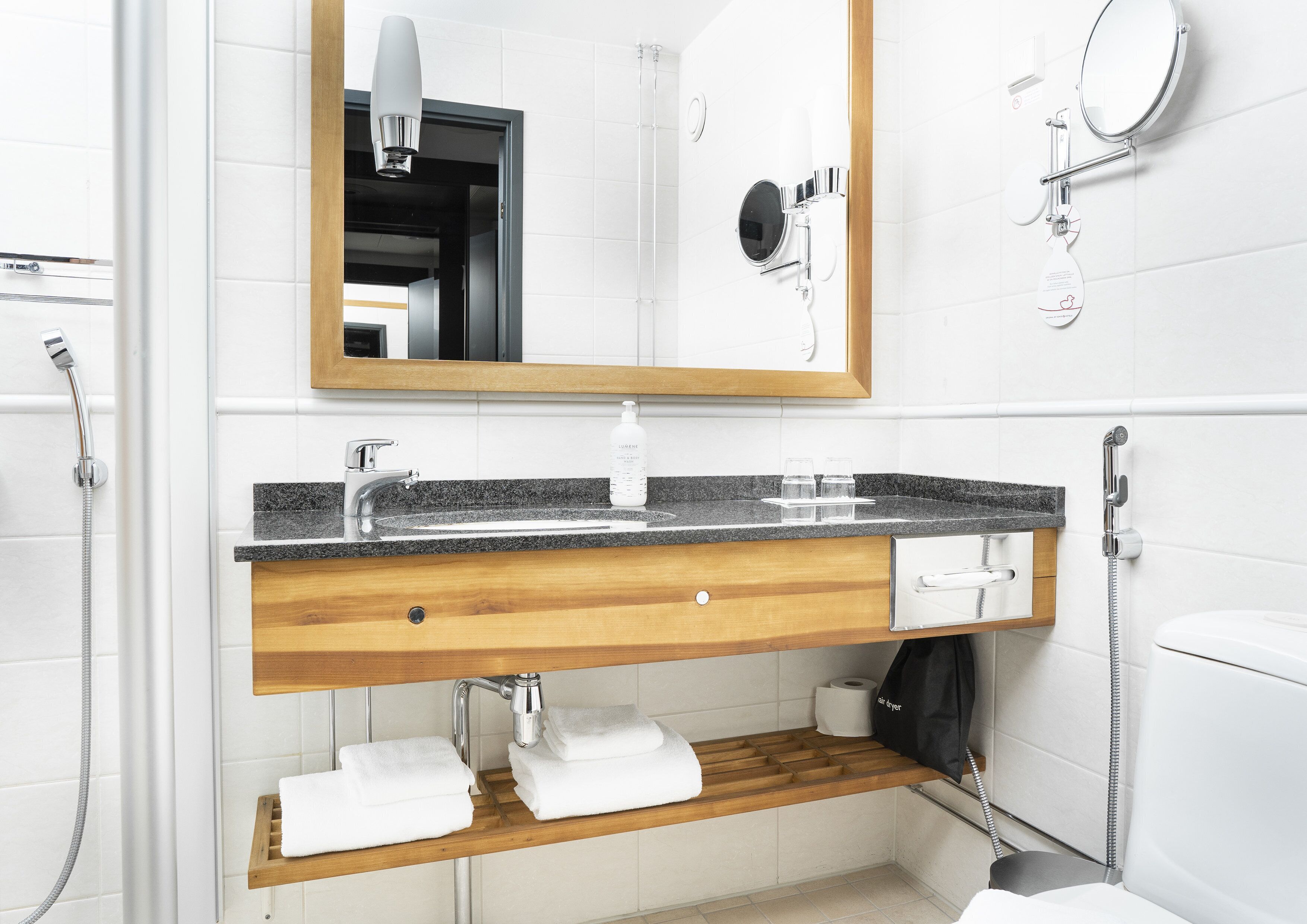 A modern bathroom with a granite countertop, a wooden vanity, a mirror, a handheld showerhead, and a toilet.