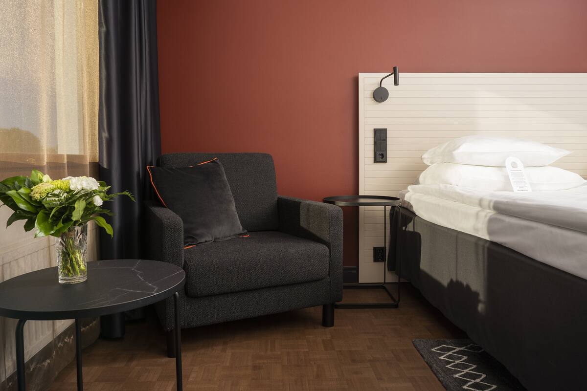 Une chambre d’hôtel avec un lit, une chaise, une petite table et un vase avec des fleurs.