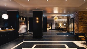 A modern hotel lobby with a reception desk, seating area, and a chandelier.