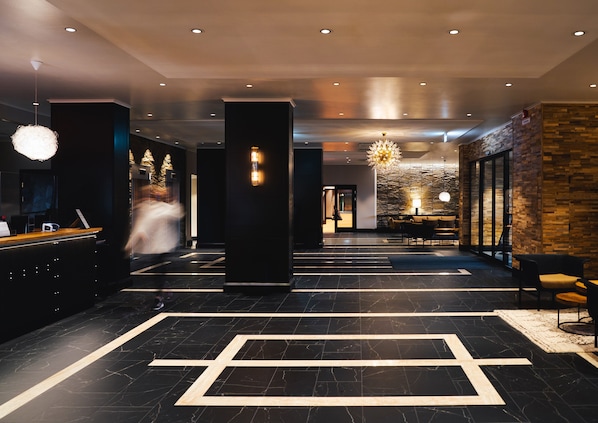 Un moderno vestíbulo de hotel con una recepción, zona de estar y un candelabro.