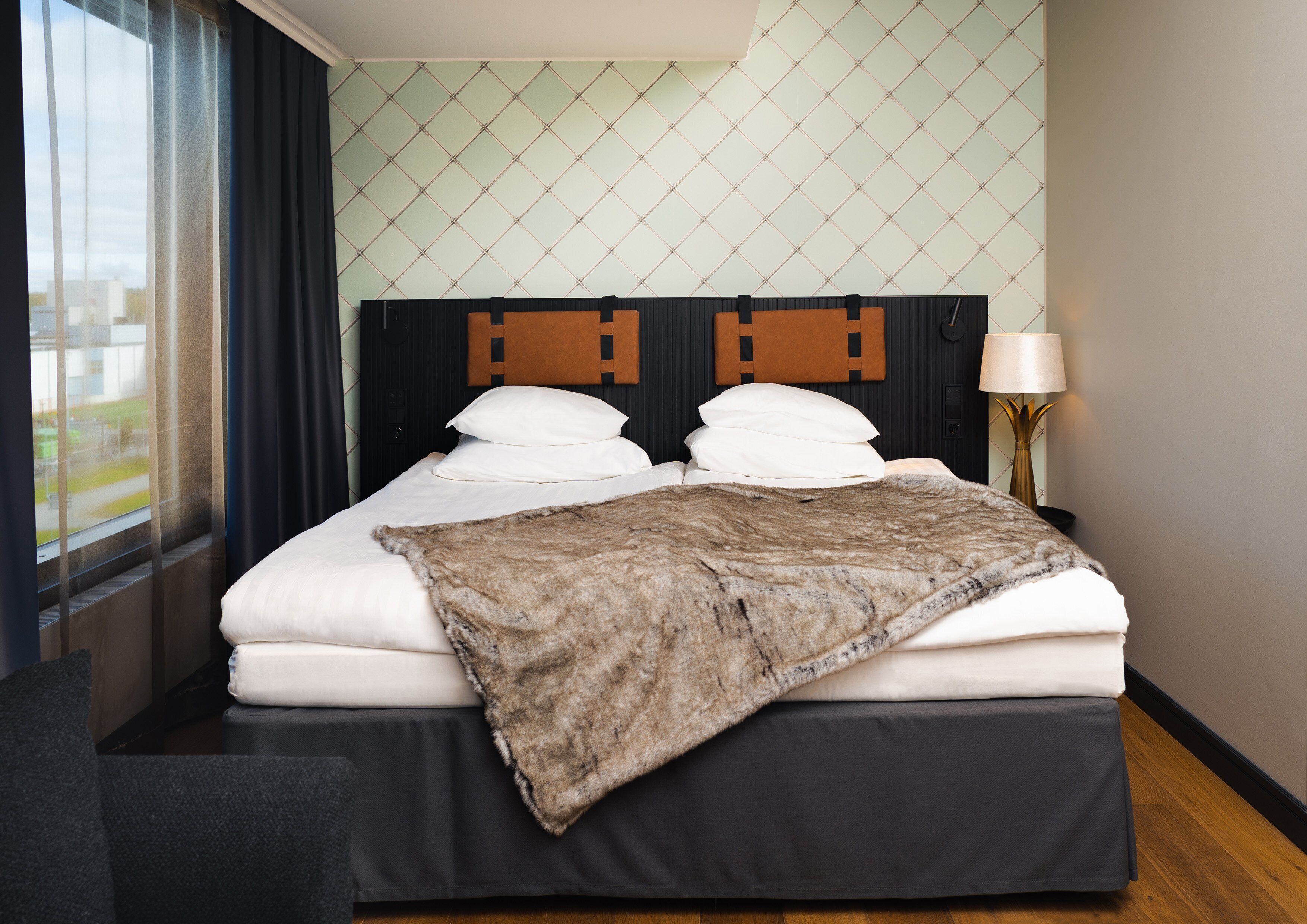 A neatly made bed with a blanket, a headboard with wooden panels, and a lamp on the side.