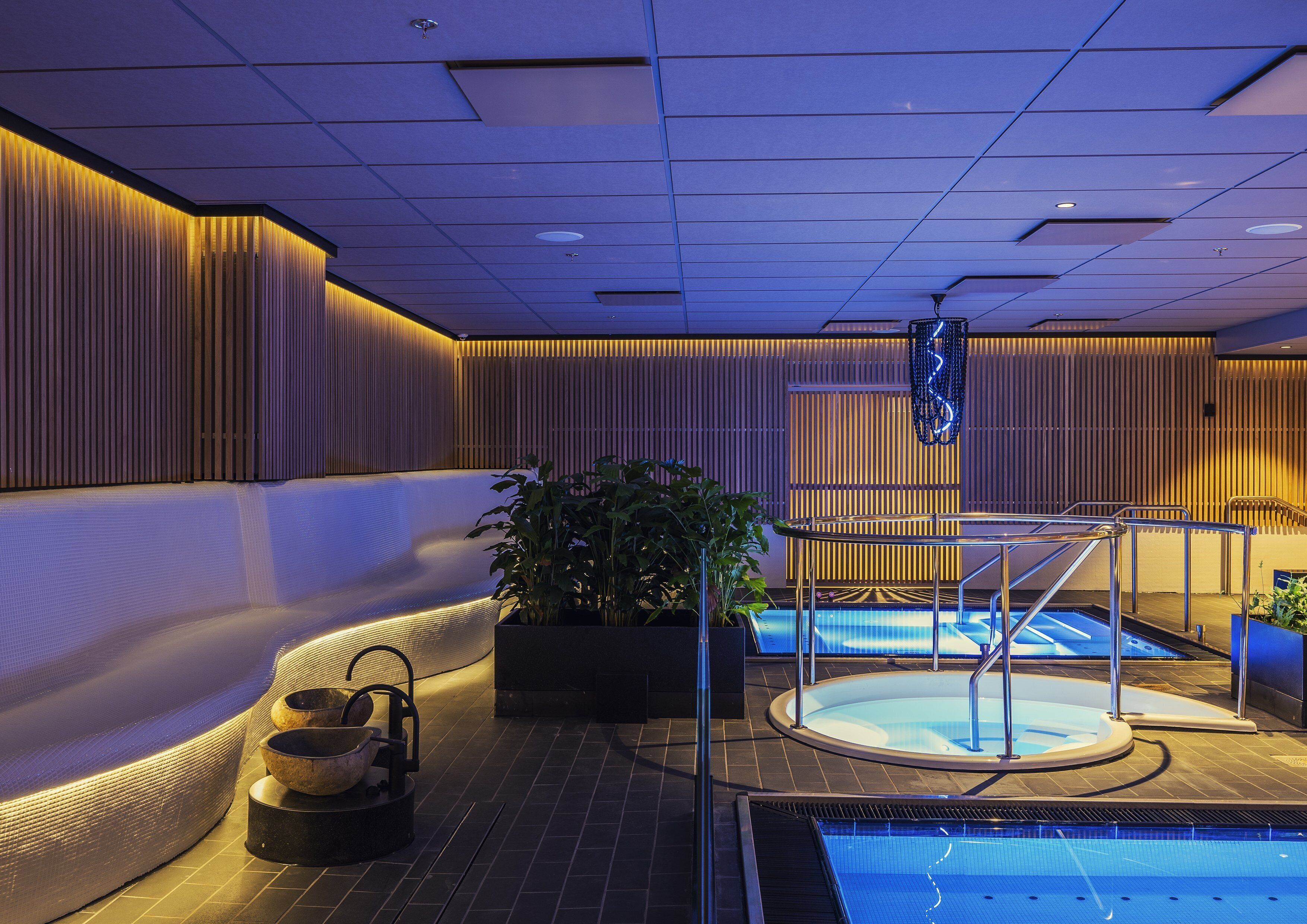 Un área de piscina interior moderna con jacuzzi, una piscina pequeña y un espacio para sentarse.
