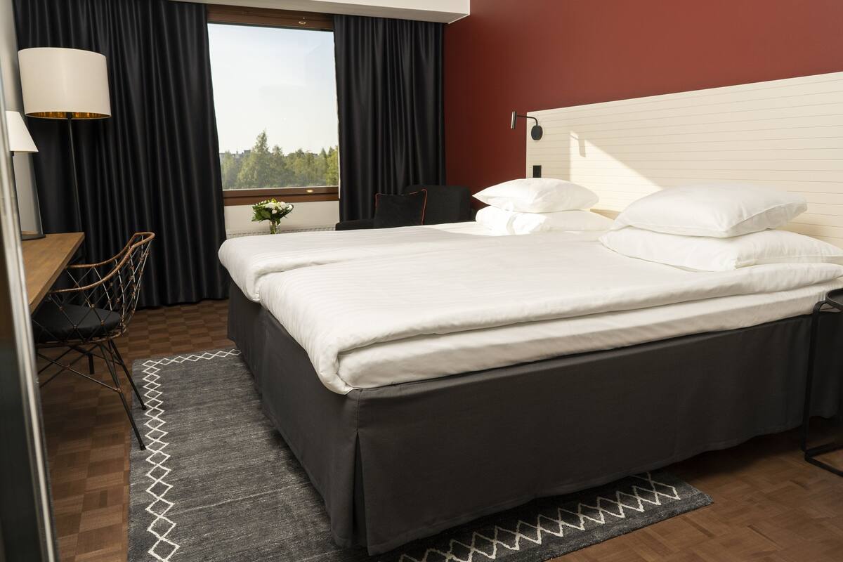 Une chambre d’hôtel avec un grand lit, un bureau, une chaise, une lampe et une vue sur les arbres par la fenêtre.