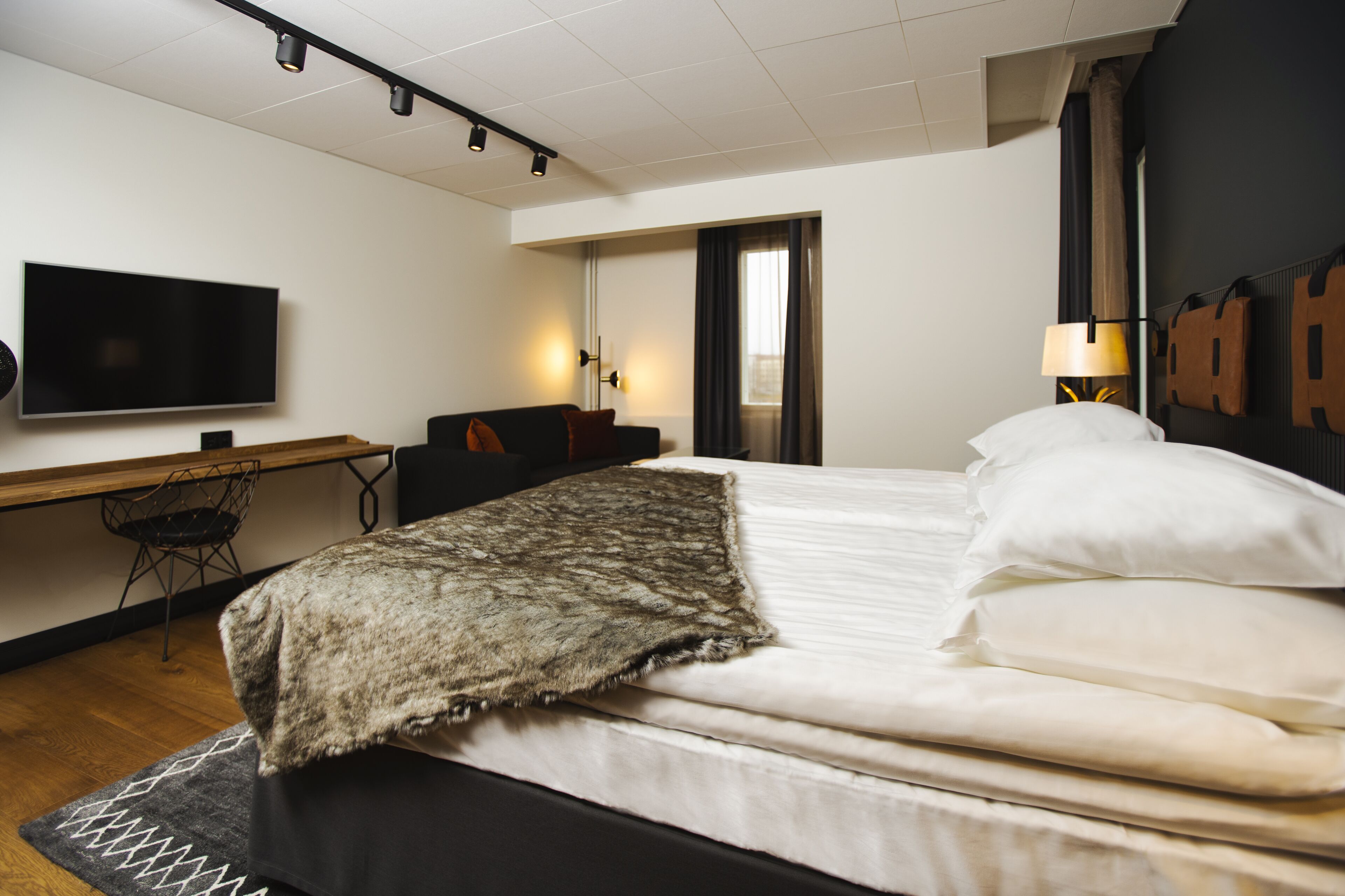 Una camera d'albergo moderna con un letto, una scrivania con una sedia, una televisione a schermo piatto e una lampada.