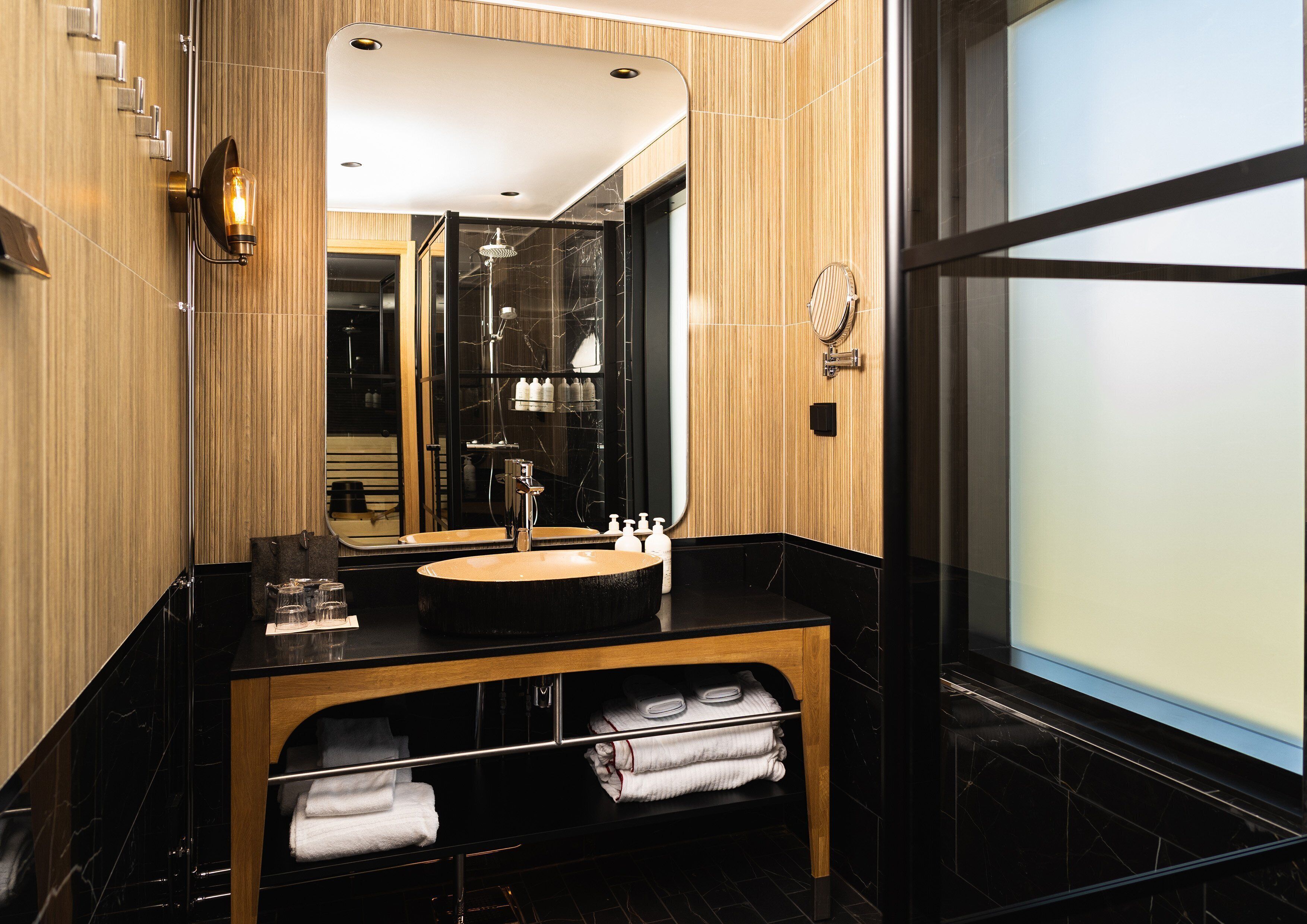 A modern bathroom with a wooden vanity, a large mirror, and a glass shower enclosure.