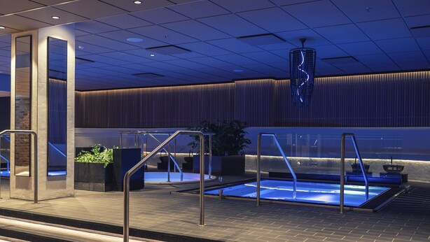 A modern indoor pool area with clear glass railings, a blue-lit water feature, and a contemporary ceiling design.
