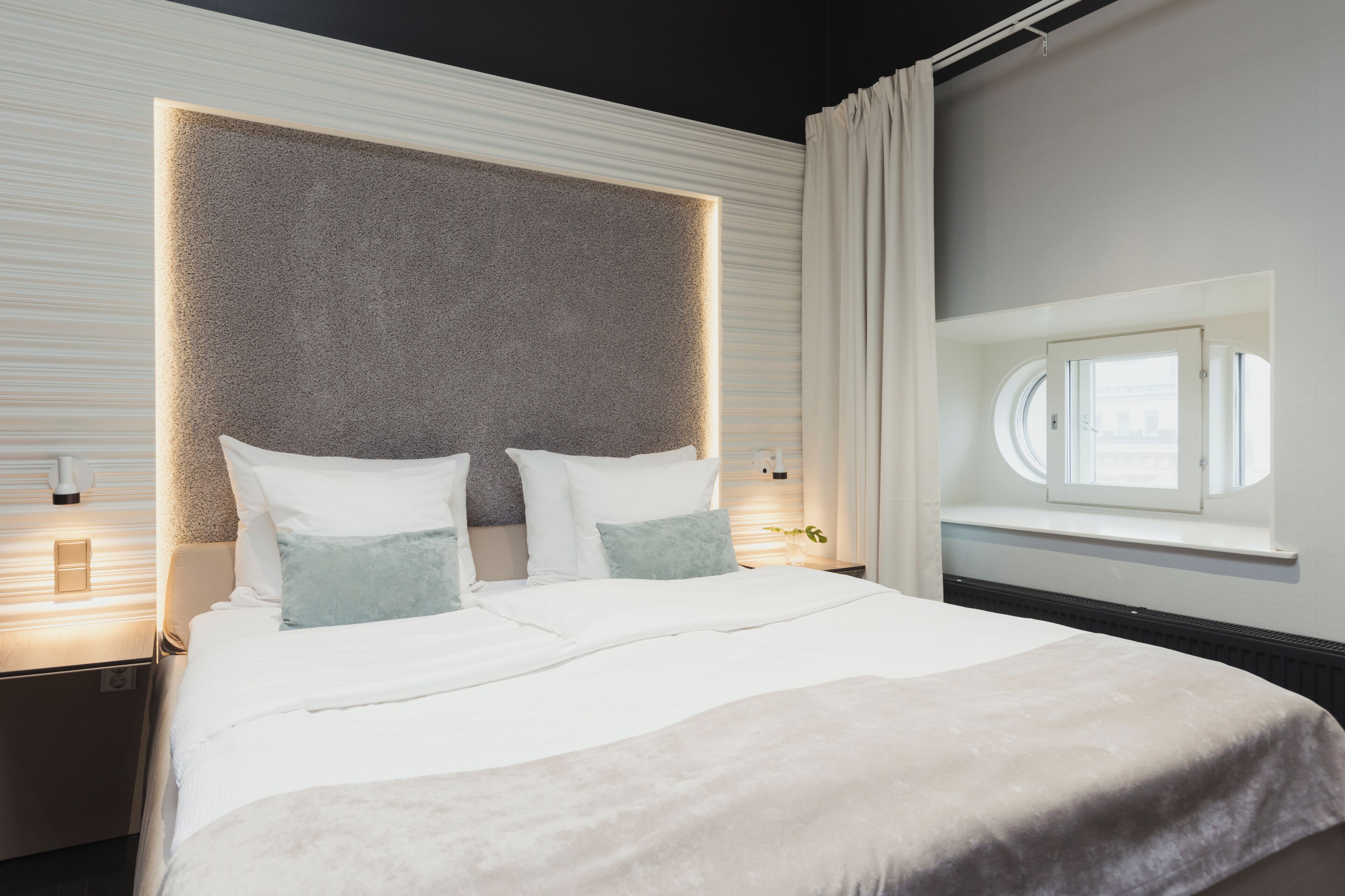 Un dormitorio moderno con una cama grande, cabecera con iluminación integrada, mesitas de noche y ventana con vistas.