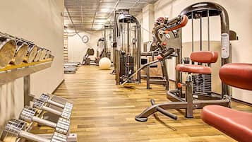 A gym with various exercise machines, a wooden floor, and a wall-mounted rack of dumbbells.