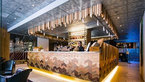 Zona bar moderna con un bancone a motivi a zigzag, elementi in legno e una scala che conduce a un livello superiore.