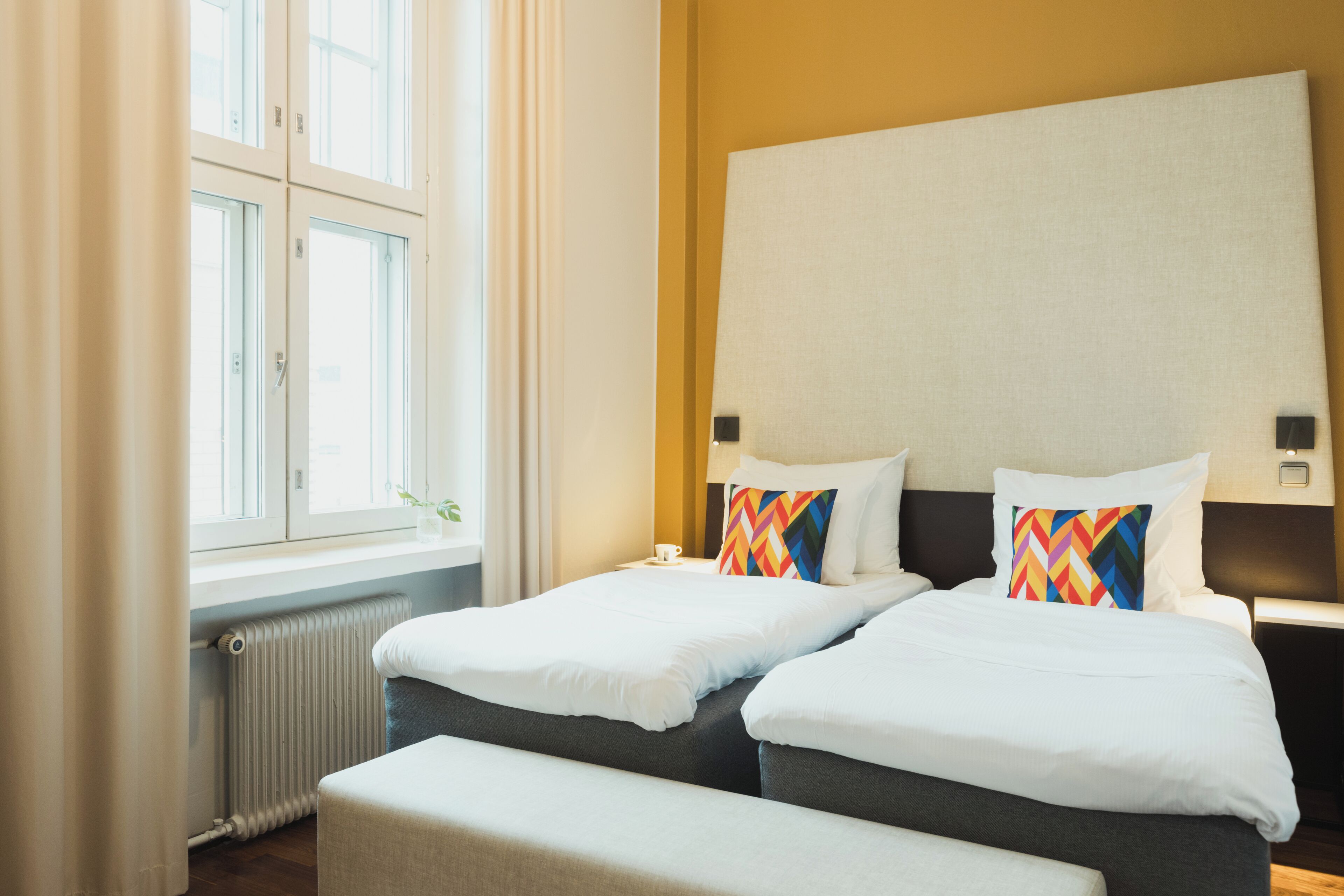 A hotel room with two beds, a large window, and a radiator.