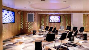 A conference room with a geometric patterned floor, black and grey chairs, and two large screens on the walls.
