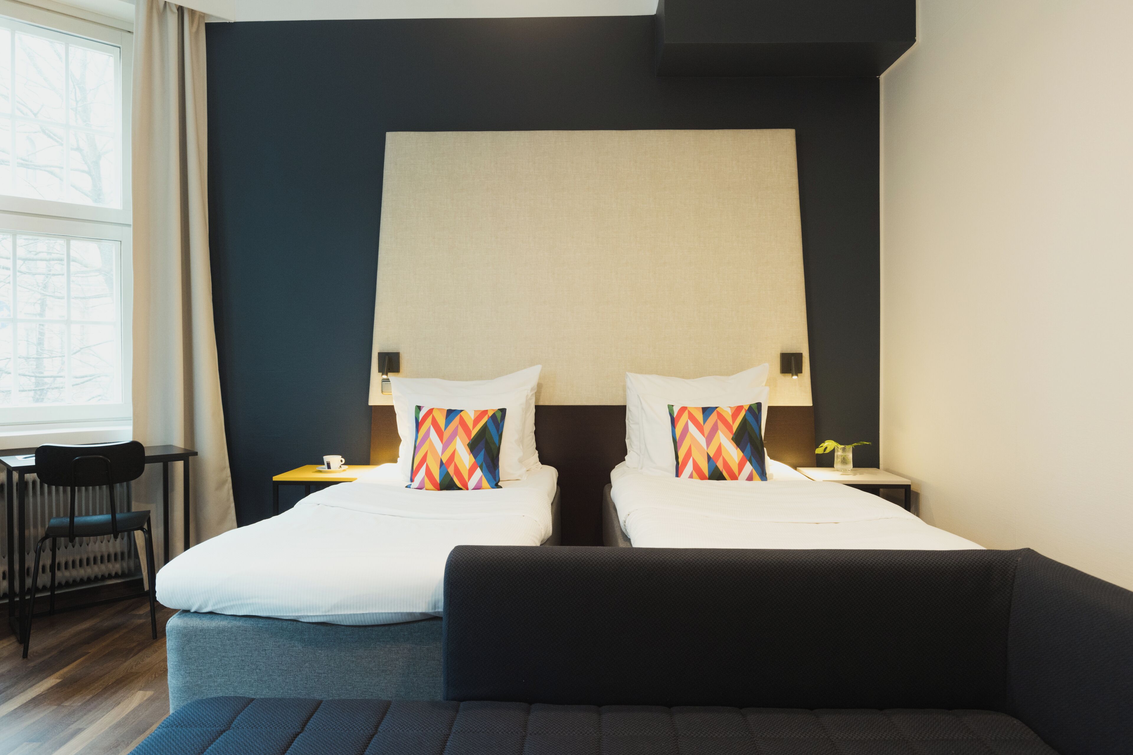 A hotel room with a large bed, two bedside tables with lamps, a desk, and a chair.