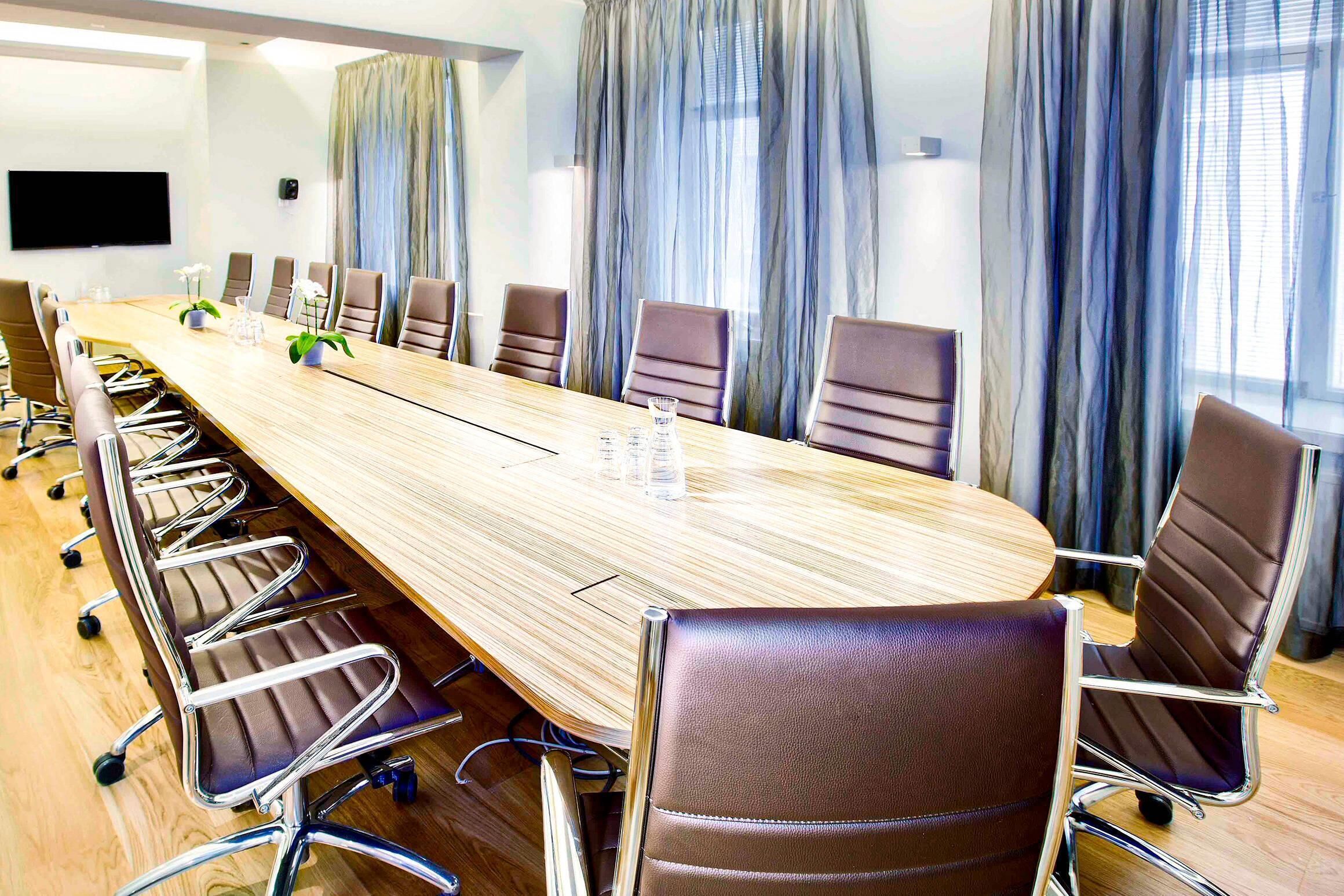 A conference room with a long table, chairs, and a TV screen.