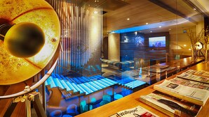 A modern interior with a wooden reception desk, a large decorative lamp, a staircase with blue lighting, and a seating area with a TV screen. - Klaus K Hotel (Helsinki)