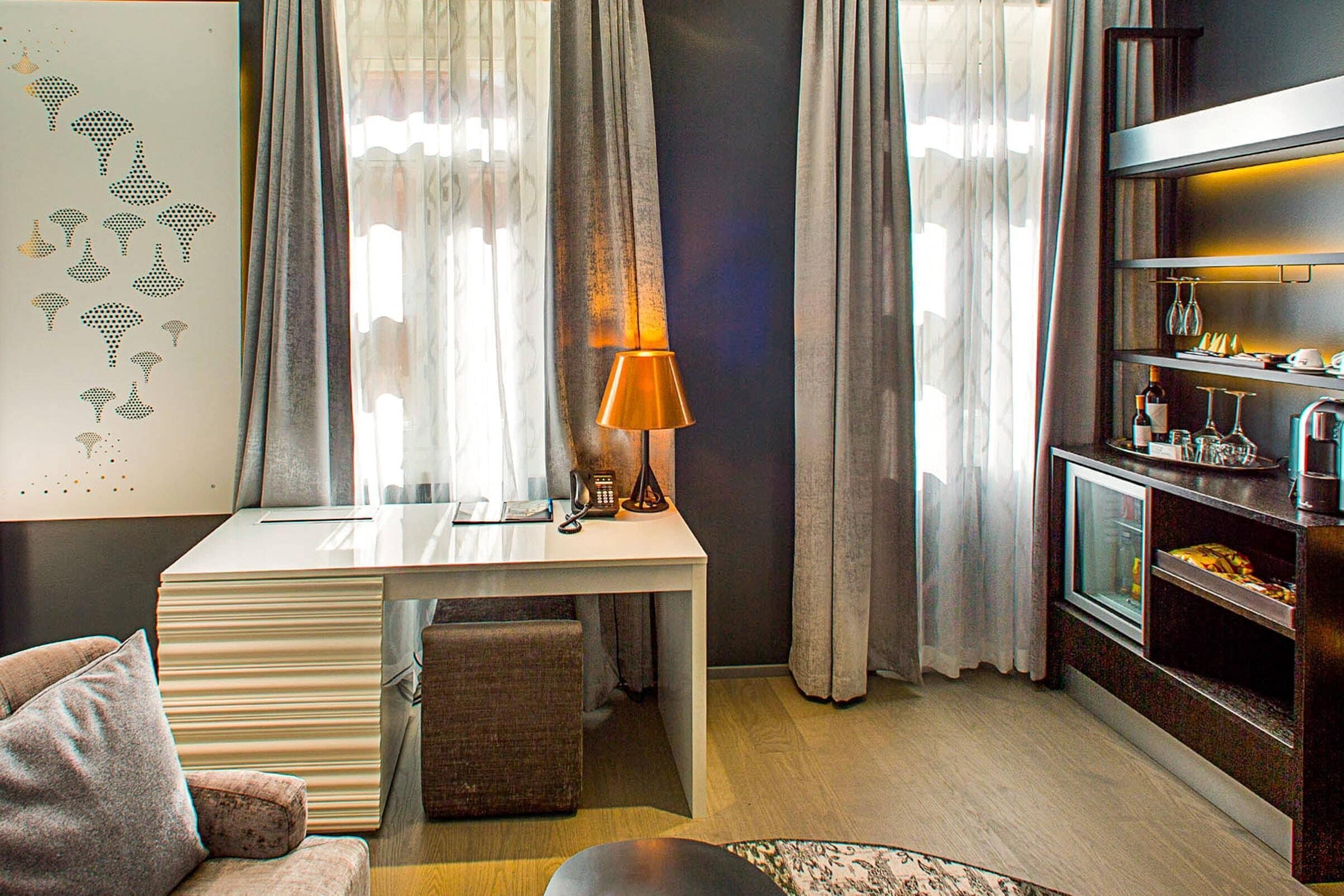 A modern living room with a white desk, a lamp, a sofa, and a TV stand with wine glasses.