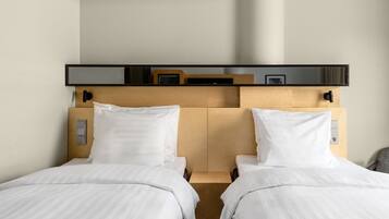 A hotel room with two single beds, a wooden headboard, a flat-screen TV, and a small bedside table.