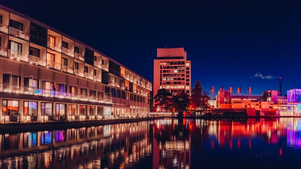 A waterfront hotel with multiple balconies, a central tower, and a reflection in the water.