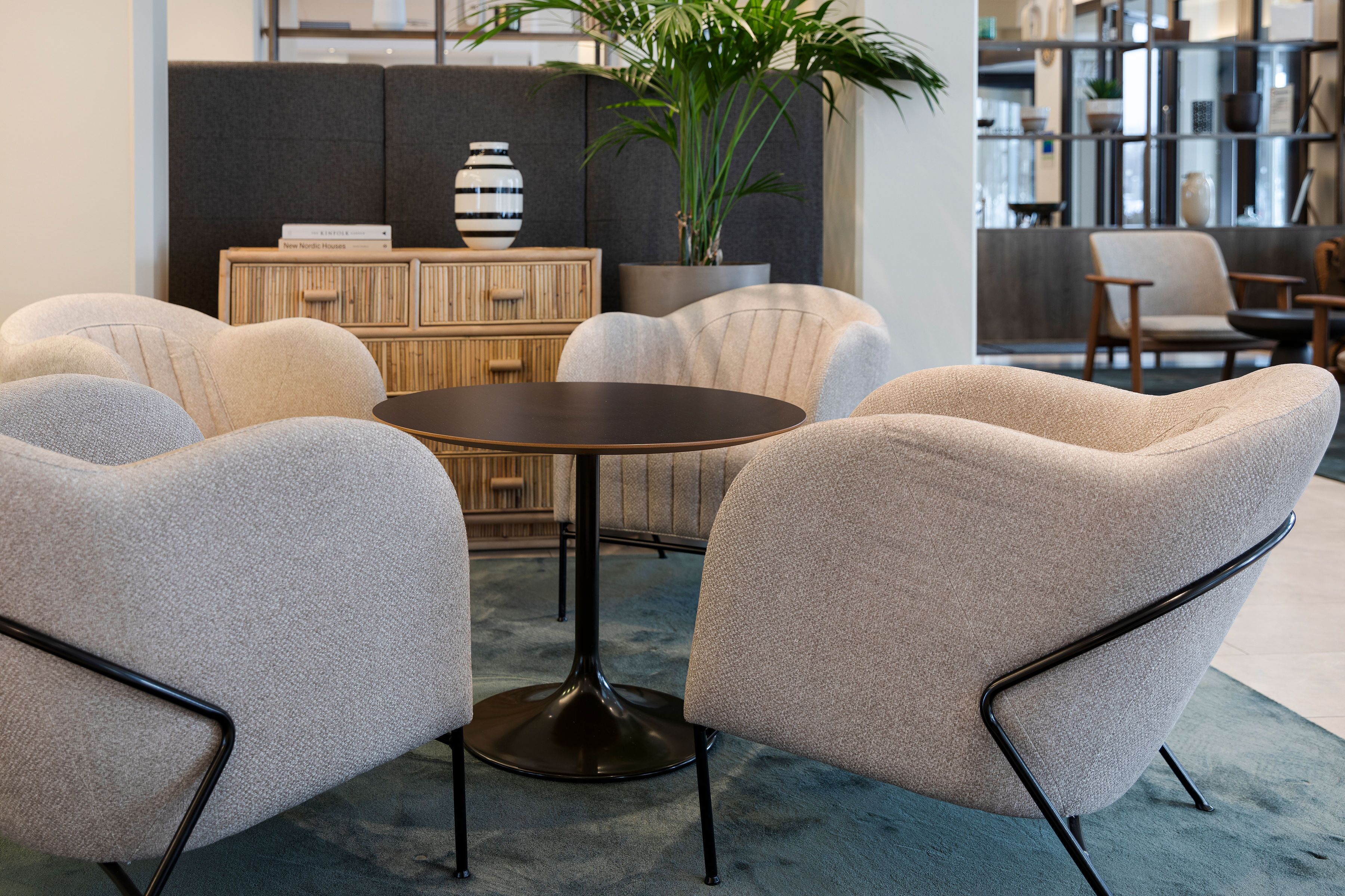 A modern living room with a round table, two armchairs, a bookshelf, and a potted plant.