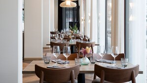 A restaurant with multiple tables set for dining, featuring a modern interior design with wooden furniture and pendant lighting.