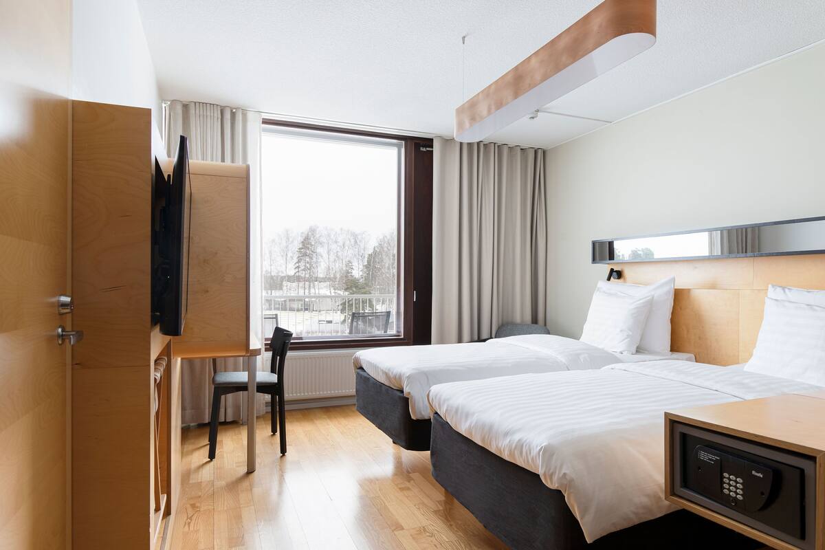 Une chambre d’hôtel avec deux lits, un bureau, une télévision et une fenêtre donnant sur des arbres.