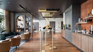 Un hall d’hôtel moderne avec un plancher en bois, un espace salon doté de canapés et de fauteuils, une table centrale aux pieds dorés et un bar avec un comptoir en bois et des éléments décoratifs.