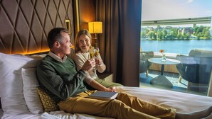Un couple est assis sur un lit, avec vue sur une rivière et la verdure environnante.