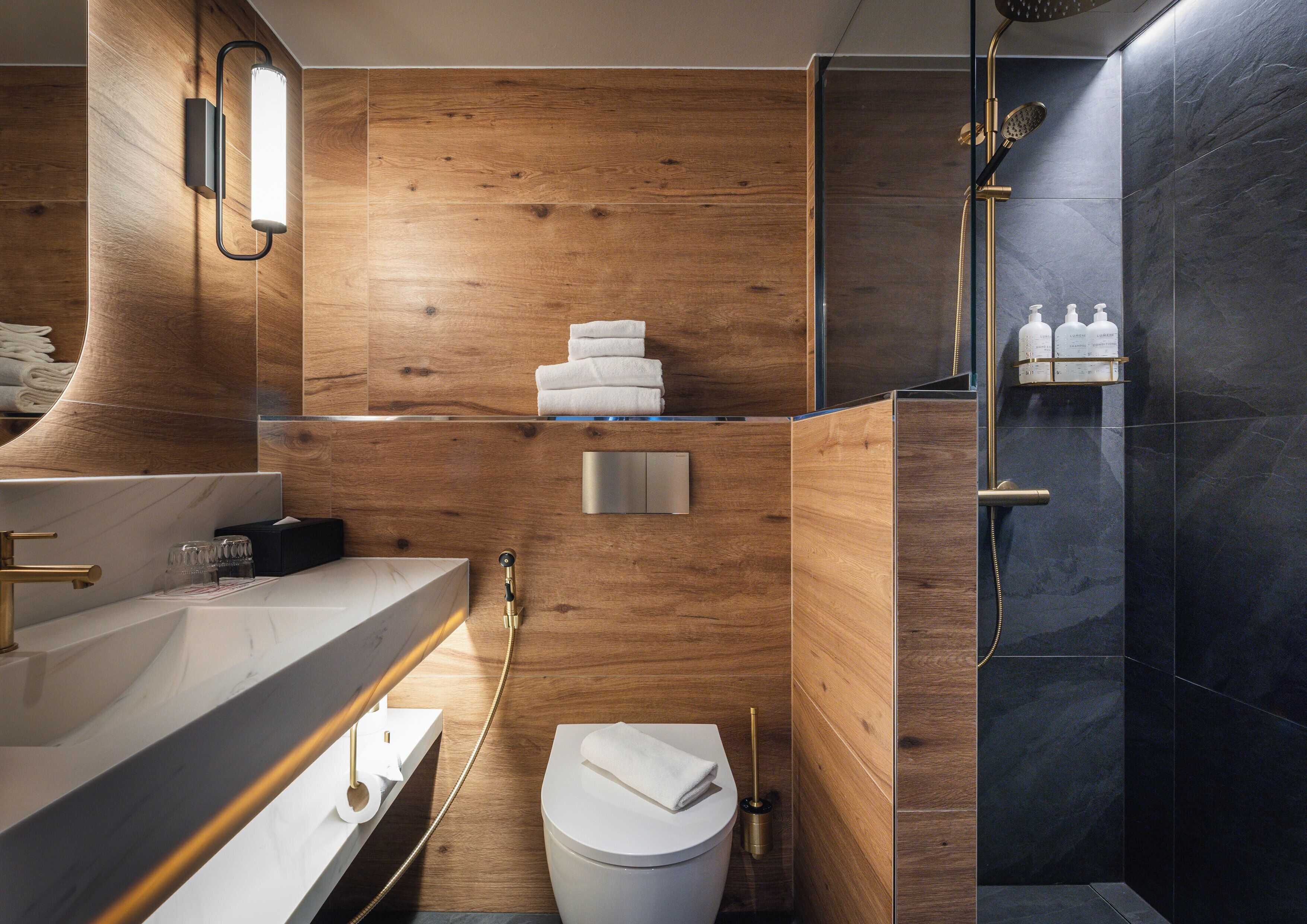 Un baño moderno con pared de madera, un lavamanos blanco, un inodoro y una zona de ducha.