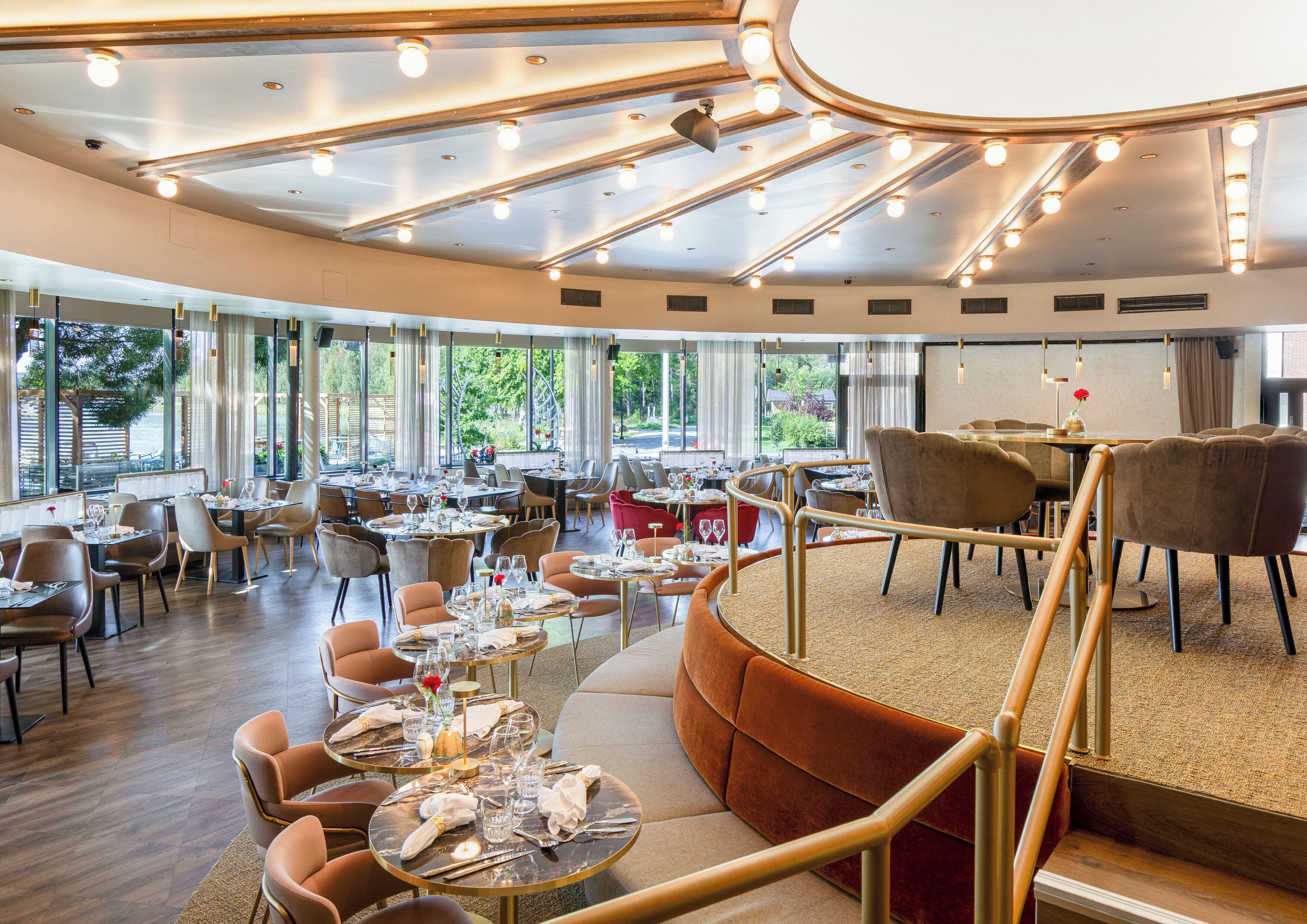 Un restaurante espacioso con varias zonas de comedor, amplias ventanas que ofrecen vistas al exterior y un diseño de techo moderno con iluminación integrada.