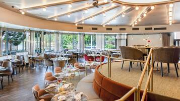 Un restaurante espacioso con varias zonas de comedor, amplias ventanas que ofrecen vistas al exterior y un diseño de techo moderno con iluminación integrada.
