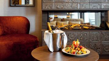 A room with a red velvet sofa, a metal bucket with a bottle of champagne, and a plate of fruit on a wooden table.