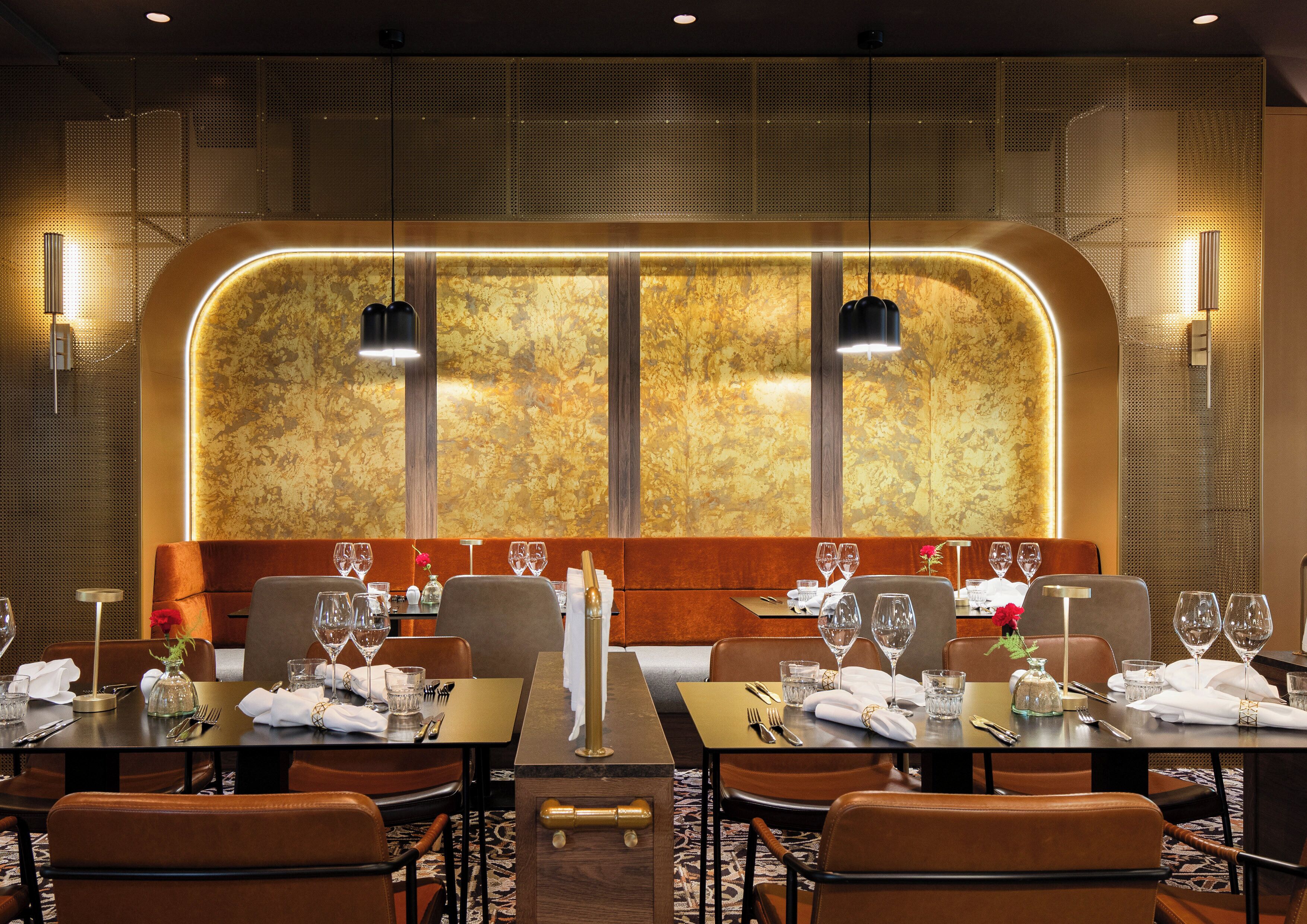 A restaurant with a modern interior, featuring a long table with multiple chairs, a decorative wall with a textured pattern, and pendant lighting.